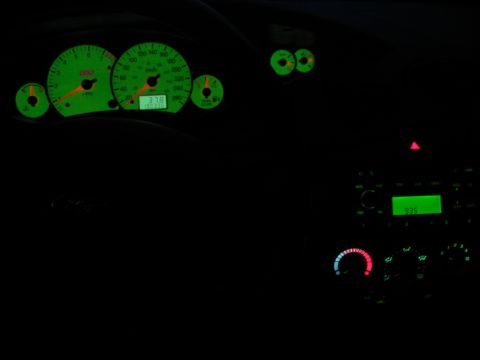 Dashboard of a 2003 Ford Focus at night, showing green illuminated gauges and radio display