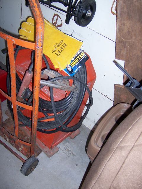 1991 Ford Bronco - Welding equipment is stored on a cart next to a brown seat and wooden wall.
