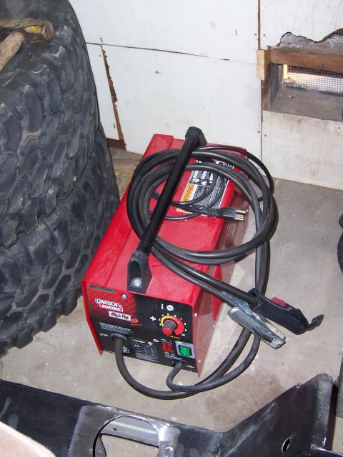 1991 Ford Bronco - A red Lincoln Weld Pak 100 welding machine sits next to a large tire and some metal framing.