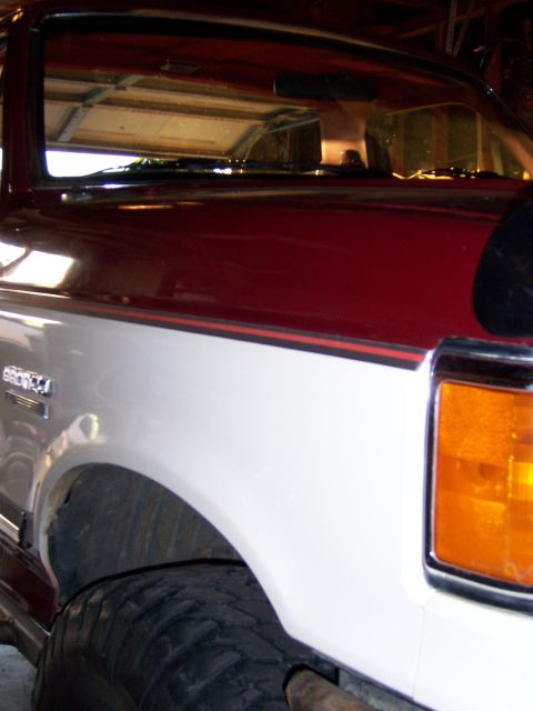1991 Ford Bronco - Close-up of a two-tone red and white 1991 Ford Bronco's front fender, showing the 'BRONCO' badge and amber turn signal light.