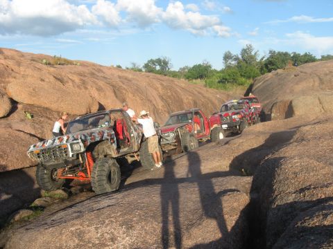 1979 Ford Bronco - Several off-road trucks navigate a rocky terrain under a partly cloudy sky.