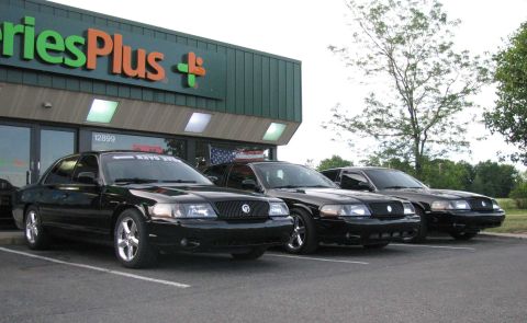 2003 Mercury Marauder - Three black 2003 Mercury Marauders are lined up in front of a store with a green and orange sign.