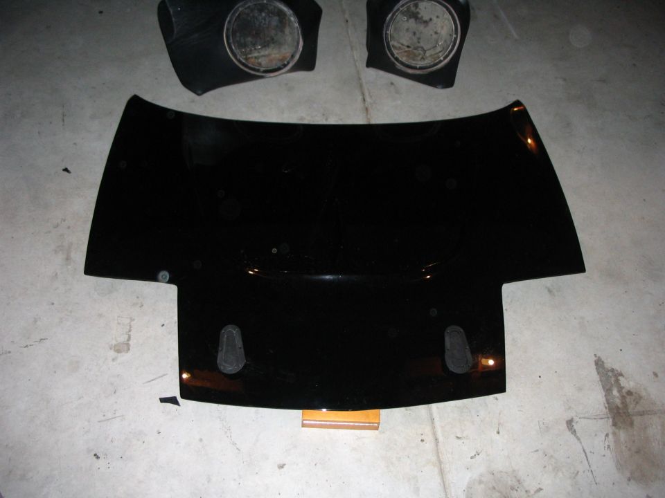 Black sports car front clip hood and two pop-up headlight assemblies on a garage floor
