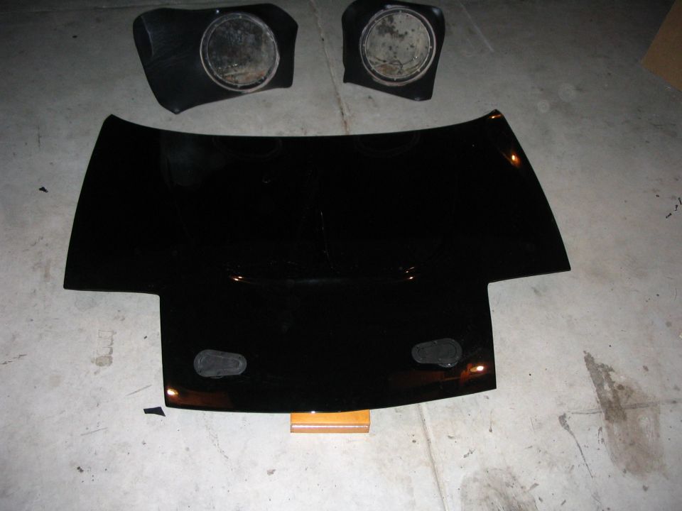 Black sports car front body panel with two pop-up headlight assemblies on concrete