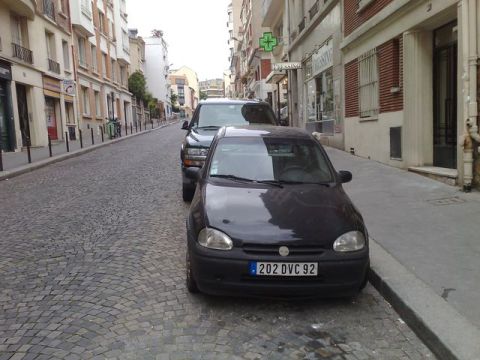 1991 Ford Crown Victoria - Two vehicles are parked on a narrow cobblestone street in a European city.