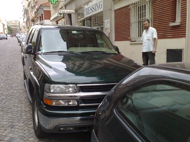 Dark green SUV, possibly a Chevrolet Tahoe or GMC Yukon, parked curbside with a man standing nearby