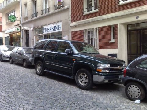 1991 Ford Crown Victoria - A dark green Chevrolet Tahoe is parked on a cobblestone street in front of buildings.