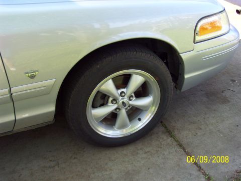 2003 Ford Crown Victoria - Front quarter panel and wheel of a silver 2003 Ford Crown Victoria, aftermarket five-spoke rims.