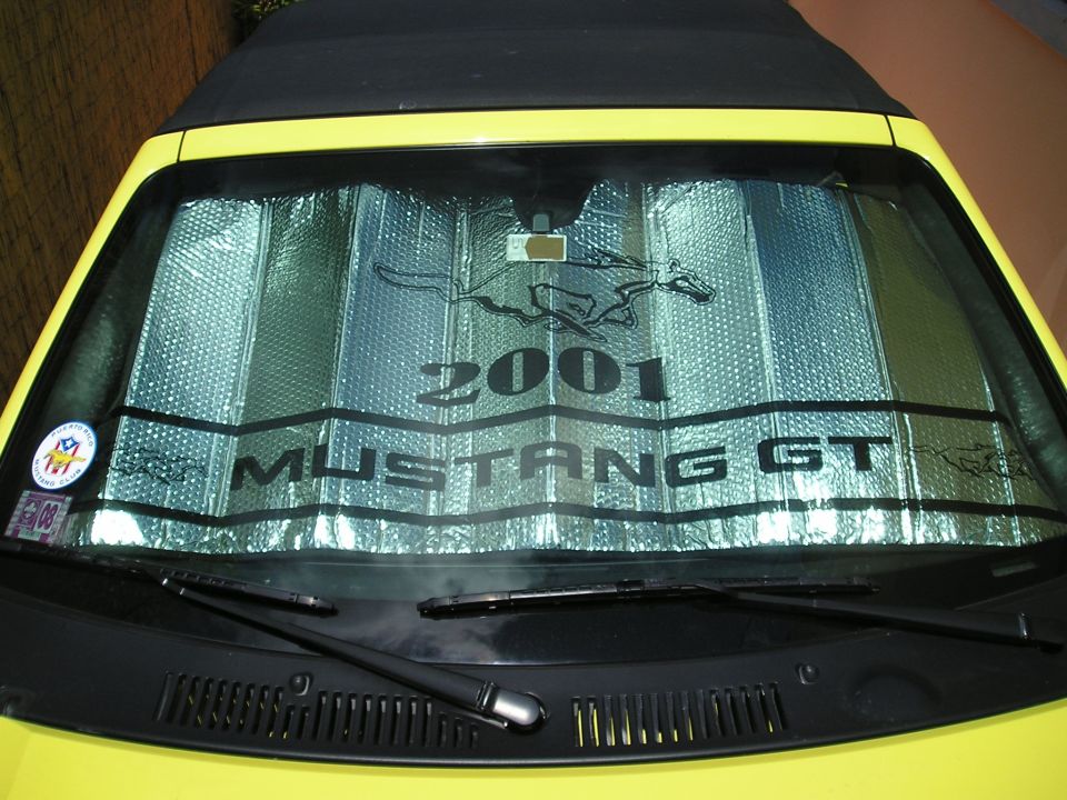 Yellow convertible Mustang GT with a sunshade displaying '2001 Mustang GT' and a running horse logo