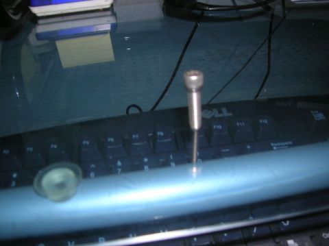 1985 Ford Bronco - A screw is placed on a Dell keyboard, with a stack of papers and a sticky note visible behind it.