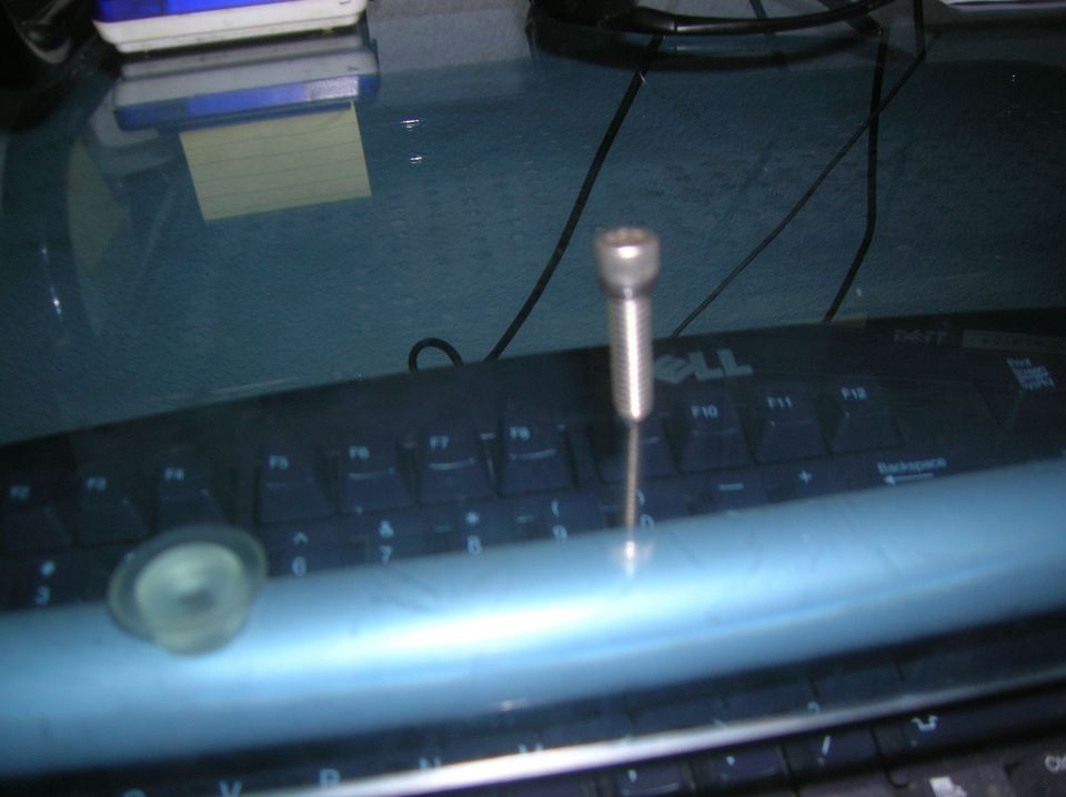 Screw standing upright on a Dell keyboard, with a sticky note pad in the background