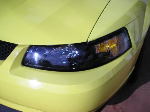 2001 Ford Mustang - Close-up of the front corner of a yellow 2001 Ford Mustang, showing the headlight and part of the grille.