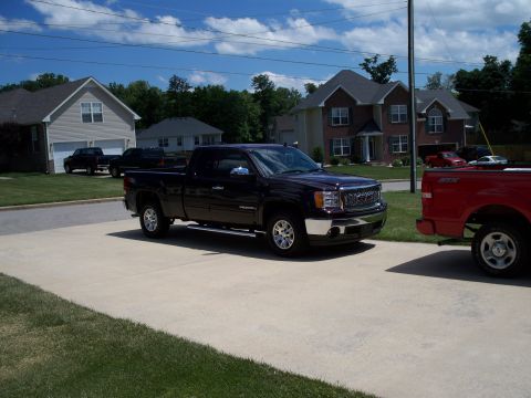 1996 Ford Bronco - A dark purple GMC Sierra pickup truck is parked on a concrete driveway next to a red Ford F-150.