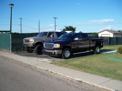 1996 Ford Bronco - A 1996 Ford Bronco is parked next to a GMC Sierra pickup truck under a clear blue sky.