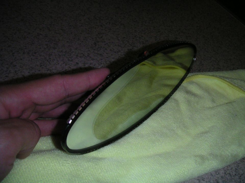 Hand holding a car's interior rear view mirror, resting on a yellow microfiber cloth