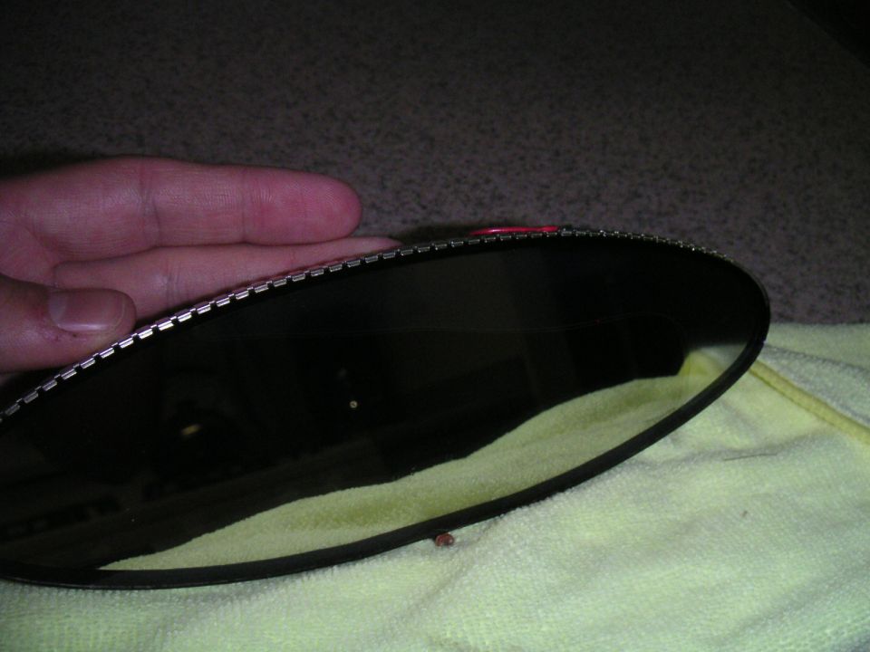 Close-up of a dark rear view mirror with a metal retaining clip edge, held by a hand
