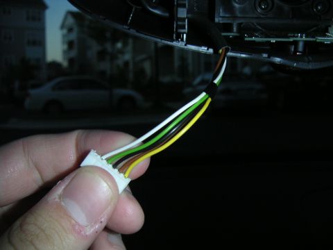 2002 BMW M3 - A close-up of a hand holding a car's interior wiring harness, with a blurred background showing houses and another vehicle.