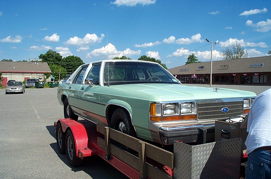 Light green sedan on a red utility trailer in a parking lot