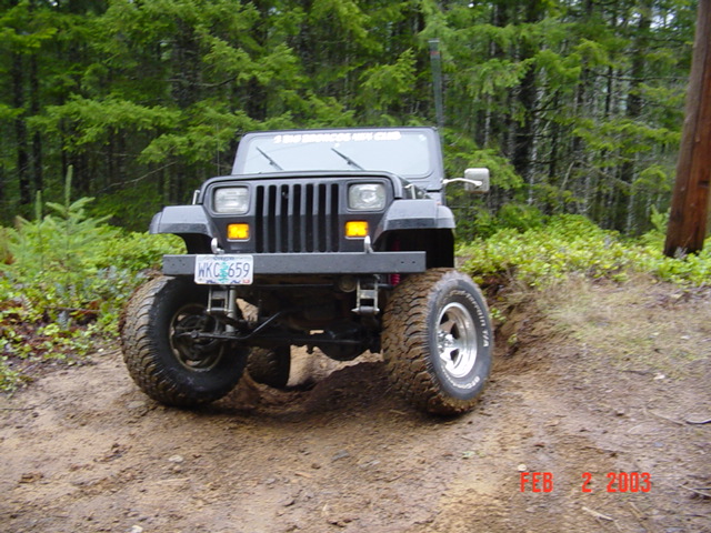 Black Jeep Wrangler on a dirt trail, front 3/4 view. Modified with large tires