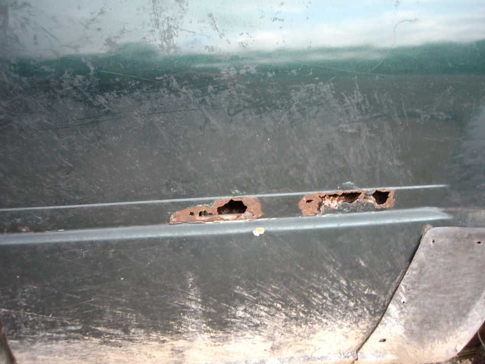 Rust holes on lower door panel of a green vehicle