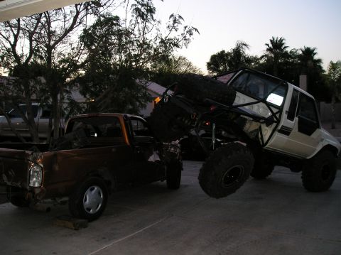 1986 Toyota Hilux - A white off-road truck with a roll cage is positioned over a damaged brown pickup truck.