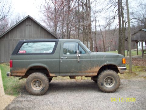 1987 Ford Bronco - This 1987 Ford Bronco is shown in profile, lifted and ready for off-road use, with a rustic building in the background.
