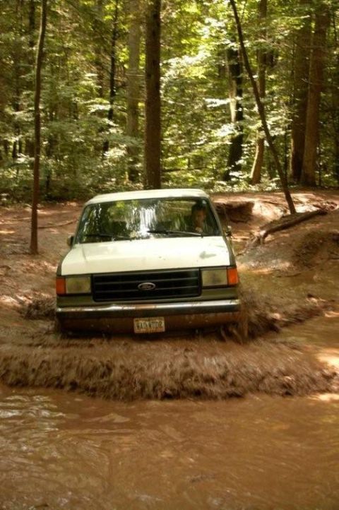 1987 Ford Bronco - A 1987 Ford Bronco navigates a muddy trail in a wooded area.