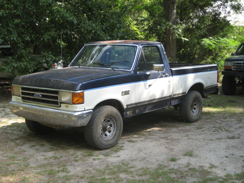 1989 Ford F-150 - A two-tone Ford F-Series pickup truck is parked on a dirt lot with trees in the background.