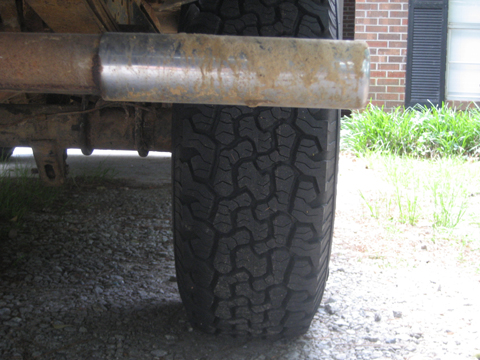 1989 Ford F-150 - A close-up view of a vehicle's rear tire and exhaust pipe, with a building and grass in the background.