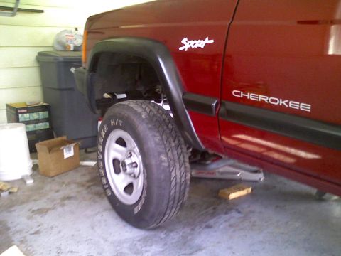 1998 Jeep Cherokee - A red 1998 Jeep Cherokee is shown from the side, with one tire lifted off the ground.