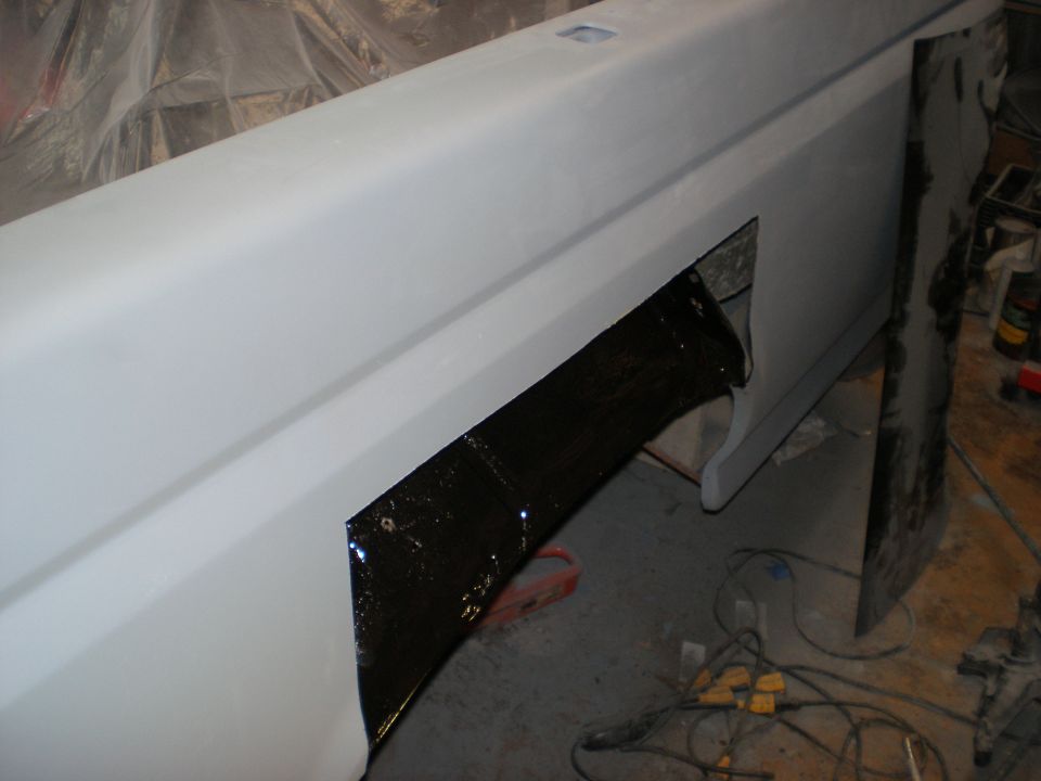 White vehicle quarter panel in body shop with large black hole cut out for custom bodywork modification