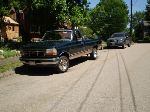 1995 Ford F-150 - A dark green Ford F-150 pickup truck is parked on a residential street, with a dark SUV behind it.