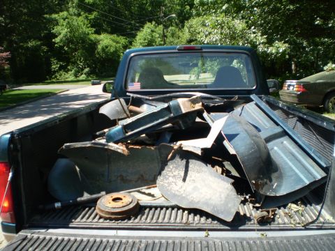 1995 Ford F-150 - A pickup truck bed is loaded with scrap metal parts, with another vehicle parked nearby in the background.