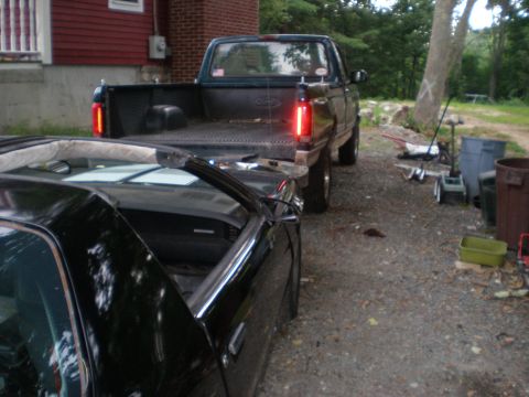 1995 Ford F-150 - A dark green Ford pickup truck is parked behind a black car in a gravel driveway.