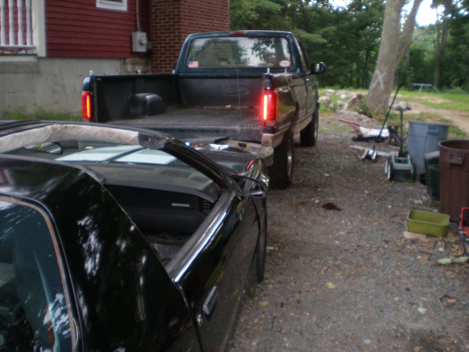 Dark green Ford pickup truck's rear end, with a black car in the foreground