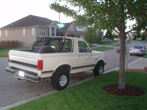 1987 Ford Bronco - White 1987 Ford Bronco with a roll cage and spare tire in the bed.