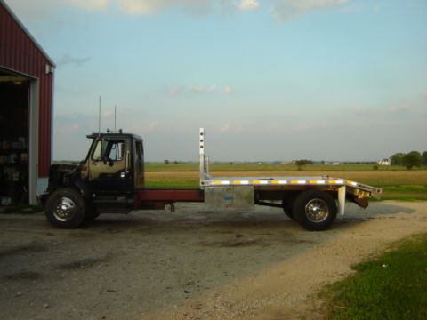 1992 Ford Bronco - A flatbed truck sits idle on a gravel driveway, with a rural landscape in the background.