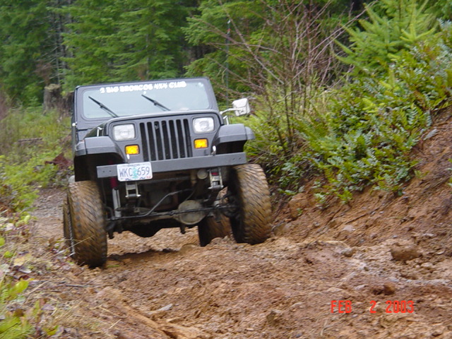 1995 Jeep Wrangler driving on a muddy, wooded trail