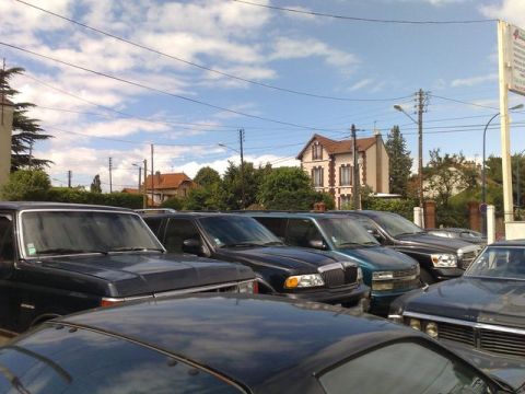 1991 Ford Crown Victoria - A row of parked vehicles under a cloudy sky, with residential buildings visible behind them.