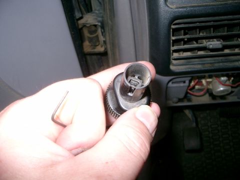 1995 Ford Bronco - A hand holds a black electrical connector with an Allen wrench, with the vehicle's dashboard interior in the background.