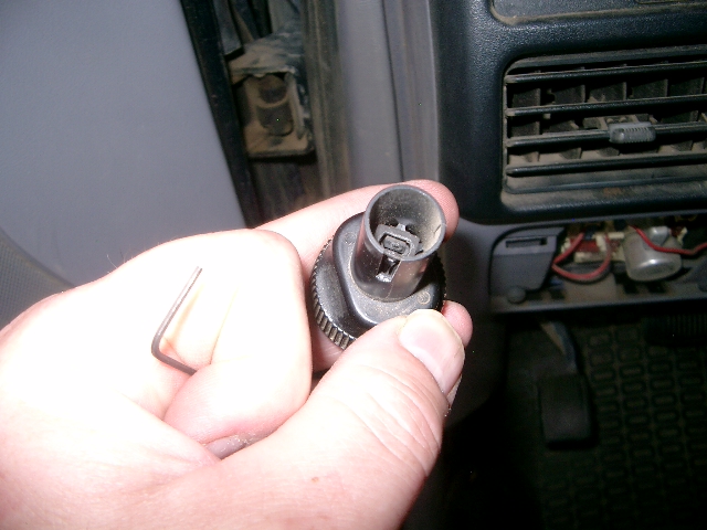 Hand holding a black electrical connector with an Allen wrench nearby, dashboard interior visible