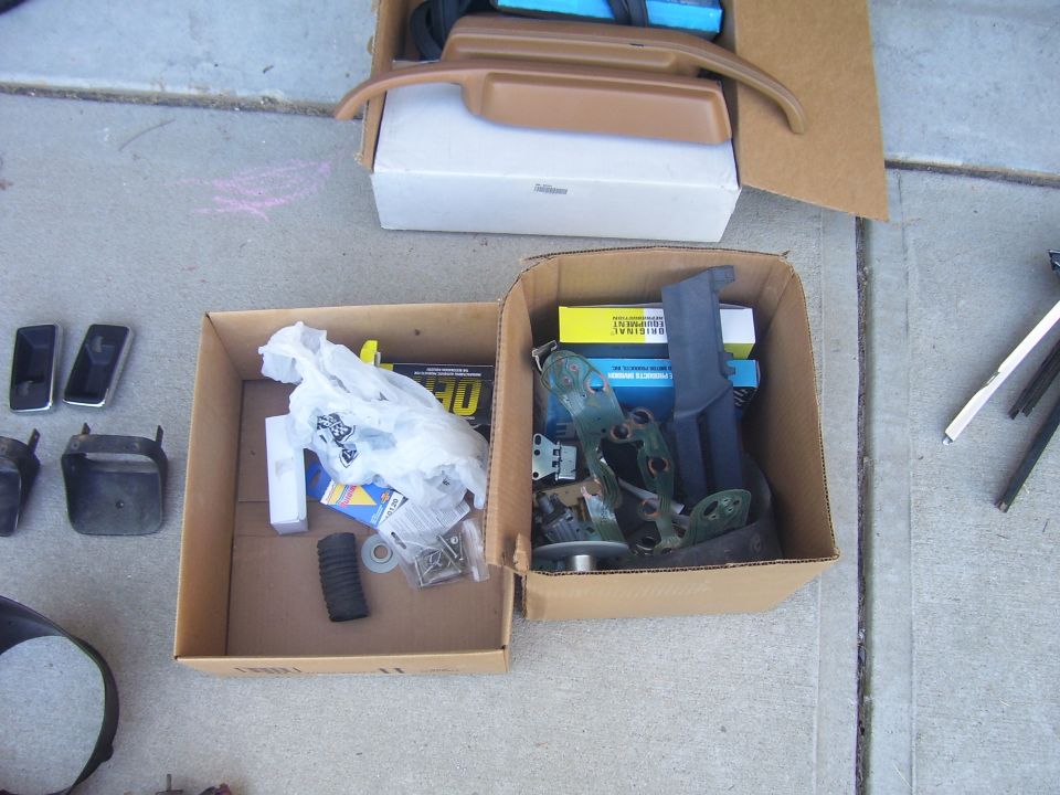 Cardboard boxes filled with assorted car parts, including trim pieces, brackets, and hardware, on a concrete surface