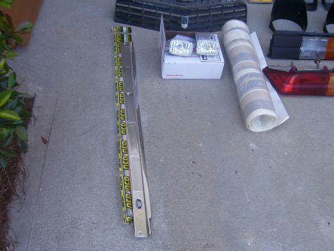 1979 Chevrolet Camaro - Various car parts, including a chrome trim piece, headlights, and taillights, are laid out on a concrete surface.
