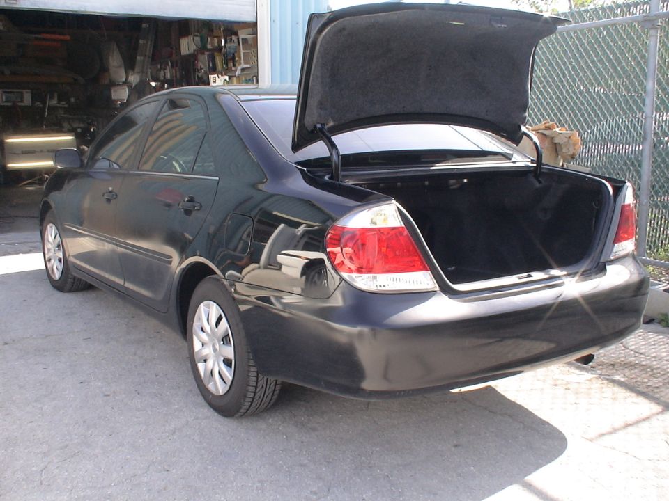 Black sedan with open trunk, rear 3/4 view. Visible damage on rear bumper