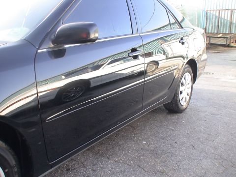 1993 Ford C-350 (Centurion Conversions) - The side profile of a black sedan is captured in this image, with reflections on its polished surface.