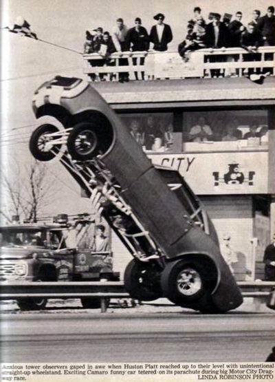 1972 Ford Ranchero - A funny car performs a wheelstand during a drag race, with spectators watching from above and a tow truck nearby.