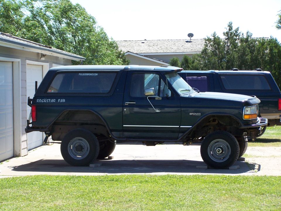 1995 Ford Bronco, dark green, lifted, with aftermarket bumpers, parked next to another SUV