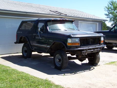 1995 Ford Bronco - This Ford Bronco is parked in front of a garage, with another vehicle visible behind it.