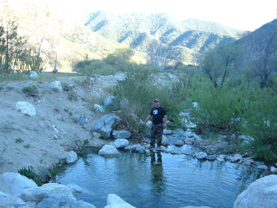 Man standing on rocks beside a creek with mountains behind