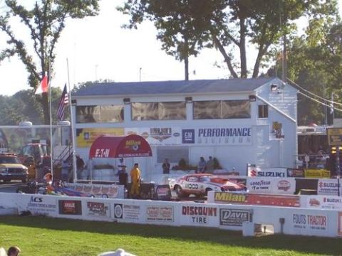 1972 Ford Ranchero - A drag racing event is underway with a race car positioned at the start line, and a building with 'GM Performance Division' signage in the…